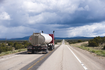 Speed up red semi truck rig with tank trailer on long road in Nevada