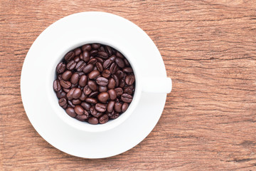Coffee beans in white cup on old brown plank floor with top view