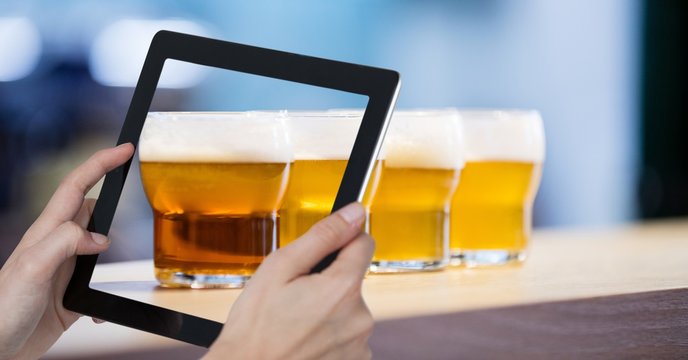 Hand taking picture of beer glasses with digital tablet in bar