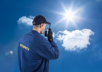 Rear view of security guard talking on walkie talkie against sky