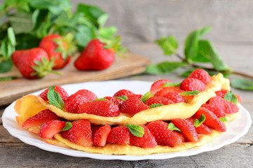 Low calorie omelette. Healthy and quick omelette stuffed with strawberries and garnished with mint leaves on a plate and vintage wooden background. Strawberry omelette recipe by diet. Closeup