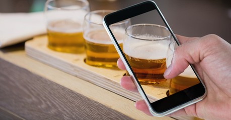 Hand photographing beer glasses through smart phone at bar