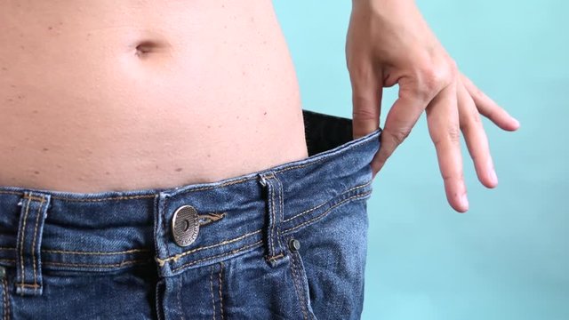 Woman losing weight after diet, slim, burning fat and flat waist. Thin girl show weight loss and old big jeans. Skinny female belly wearing too large pants. Getting in shape and reaching the goal