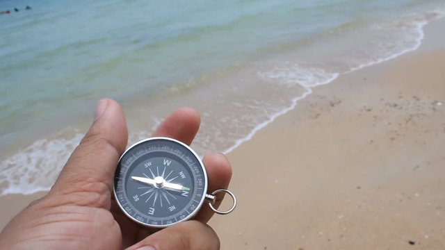 Close up shot hand of mand holding a compass on the  sand beach with nature sea and wind ambient sound
