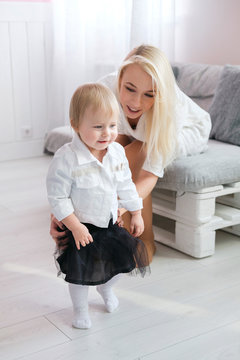 Adorable baby boy making first steps with mother at living room