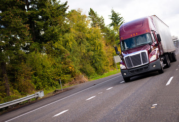 Burgundy modern semi truck and reefer trailer in straight wide highway