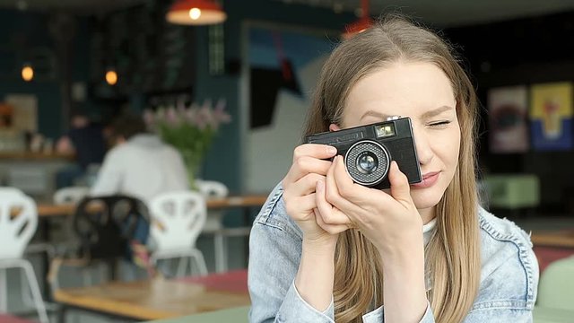 Beautiful girl doing photos on old camera and smiling while sitting in the bistro
