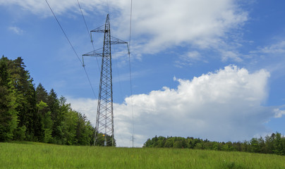 Obraz premium electrical power line pillar on meadow in front of blue sky and clouds
