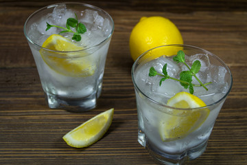 Refreshing beverage with lemon, ice and mint leaves in glass, isolated on wooden background