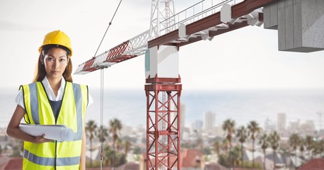 Female architect holding blue prints while standing by crane