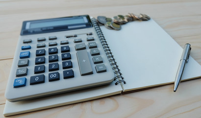 Open Notebook with silver pen and calculator next to coins on wooden table for background, copy space, flat lay. Close up.