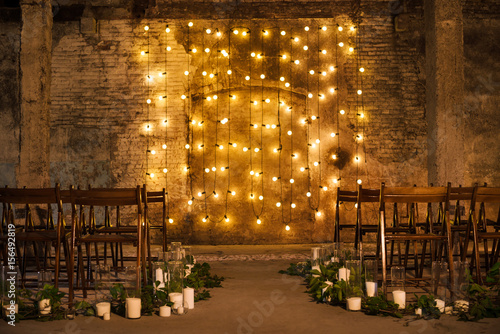 Wedding ceremony decorations in loft grunge surround. Light bulb garland, candles, glass and chairs