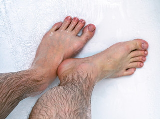 Men's hairy legs in the bathroom. A man washes in the shower