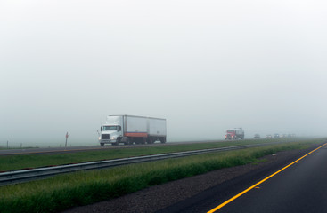 Caravan of big rigs semi trucks on the foggy highway