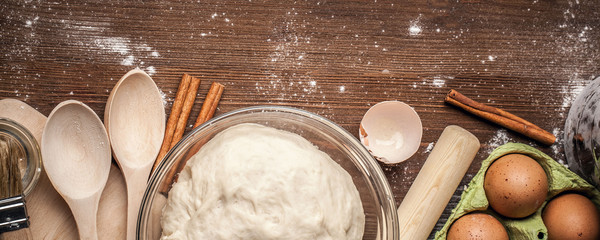 Cooking yeast dough for buns, butter, eggs, cooking equipment, flour on a wooden table. Top view with copy space, mockup for menu, recipe or culinary classes. Baking background.