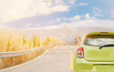 Woman hand holding a scarf out of car window and driving on Country Road With sunlight