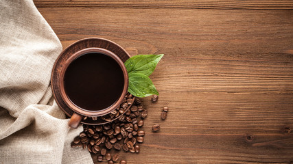 Hot coffee in a clay cup and a plate, whole or ground coffee beans lie on a brown wooden table