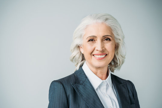 portrait of smiling senior businesswoman in suit isolated on grey