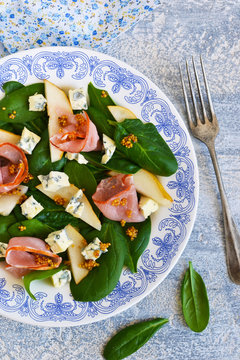 Salad with spinach, blue cheese, ham and pear sauce on a concrete background