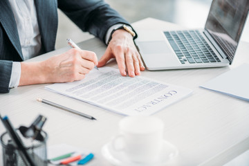 partial view of businesswoman sitting at workplace and signing contract