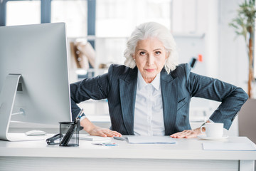 Confident aggressive senior businesswoman sitting at workplace and looking at camera