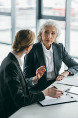 two businesswomen with clipboard discussing business project on meeting in office