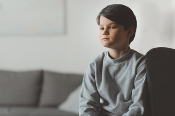 pensive little kid boy sitting on sofa at home