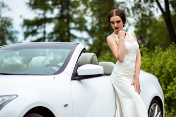 gorgeous bride with fashion makeup and hairstyle in a luxury wedding dress near white cabriolet car