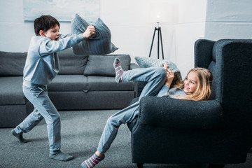 Adorable little children in pajamas having pillow fight at home