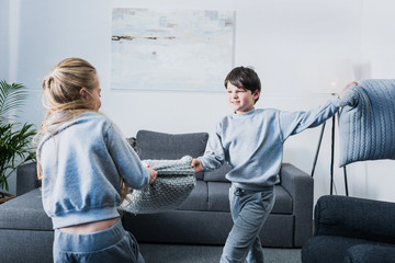 Cute little siblings in pajamas fighting with pillows at home
