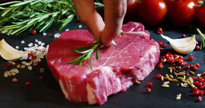 Beautiful juicy fresh meat steak on a table with salt, rosemary, garlic, and tomato on a black background, top view. Concept: fresh & natural products, bio products, meat products, organic, nutrition.