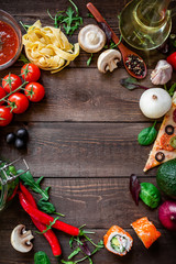 Frame made of vegetables, pizza, sushi rolls, tomato, pasta, olives and sauce on wooden background. Food concept for menu. Flat lay. Top view.