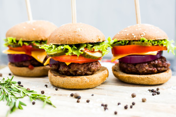 Close-up on a wooden board three beef burgers, with skewers, crispy loaf, lettuce, cheese, tomatoes, cutlets, cucumbers, onions, dark background, delicious, fast food, bright, trendy food, restaurant