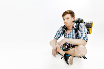 Young tourist is sitting with backpack on white background. traveler is preparing for hike