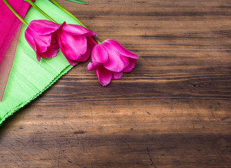 Pink tulips, floral arrangement on wooden background with green paper and space for message. Background for Mother's Day, 8 March and other greeting cards or invitations for lovely women. Soft focus.