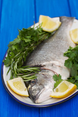 raw fish with herbs and lemon on dish on wooden background