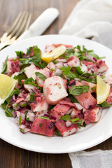 octopus salad with lemon on white dish on wooden background