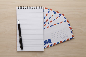 Air mail envelope, notepad and pen on the wooden table