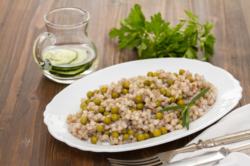 buckwheat with peas on white dish on wooden background