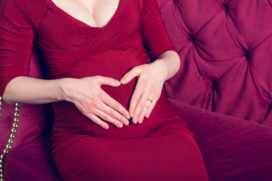 Belly of a pregnant woman with the hands of the mother's heart