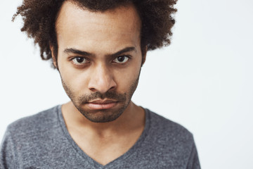 Obraz premium Close up of displeased african man looking at camera brutally. White background.