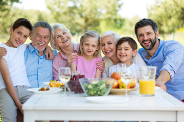 Family sitting at table outdoors, smiling
