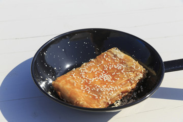 Phyllo wrapped feta cheese appetizer with honey and sesame seeds, Traditional greek dish on the white wooden table background served by the sea,