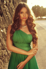 Outdoor portrait of young beautiful gorgeous girl in luxury evening green dress posint at the street. Summer fashion photo