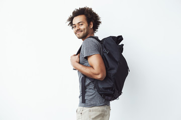 Handsome african man with backpack smiling standing in profile. White background.