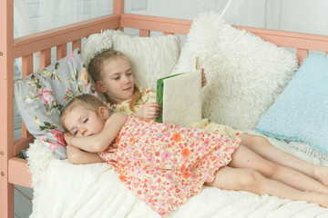 Older sister reading a book to her younger sister