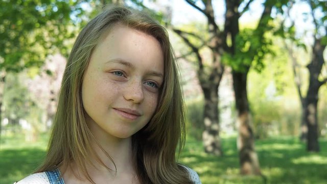 Emotions of a teenage girl. The girl's face is close-up. A beautiful face with freckles. A teenage girl smiles in the park.