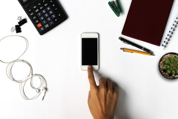 Men's hands are using a smartphone. White office desk with smartphone with black screen, pen, and supplies. Top view with copy space.