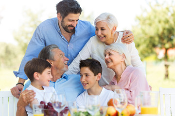 Family sitting at table outdoors, smiling

