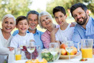 Family sitting at table outdoors, smiling
